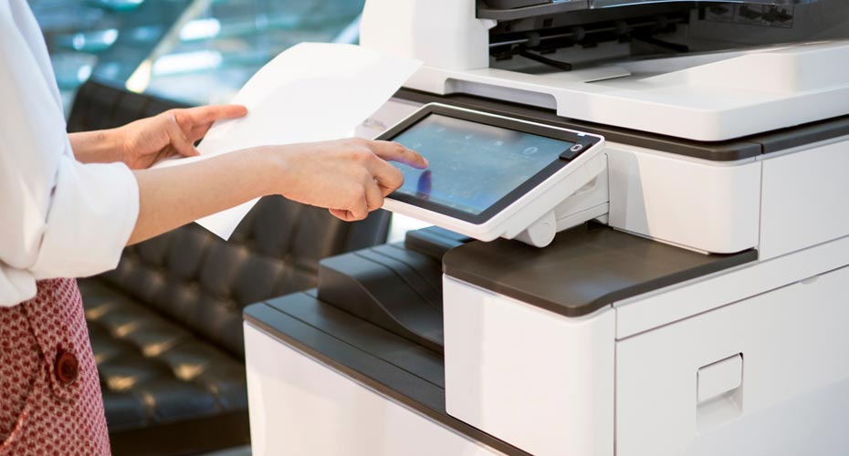 Hands interacting with the angled, color touchscreen display of an enterprise-level office printer.